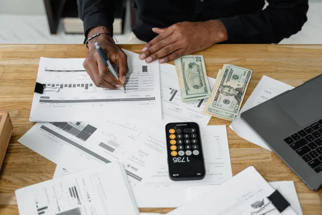 Man working on financial reports with calculator, money, and laptop on a desk. An email software budget template with reforecast triggers and stop rules