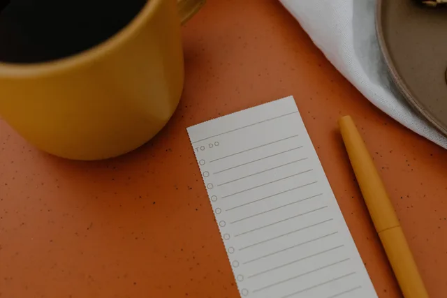 Flat lay of a mug, to-do list, and pen on an orange surface for planning inspiration. Email marketing software planning template: stop and restart