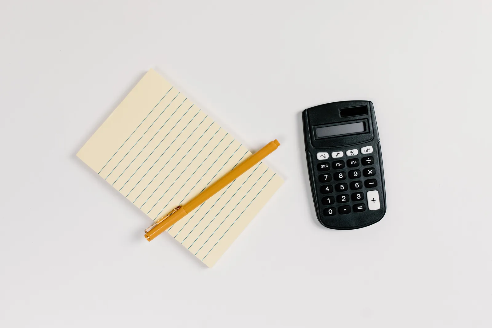 Minimalist flat lay of a calculator and lined notepad with a gold pen on a white surface.