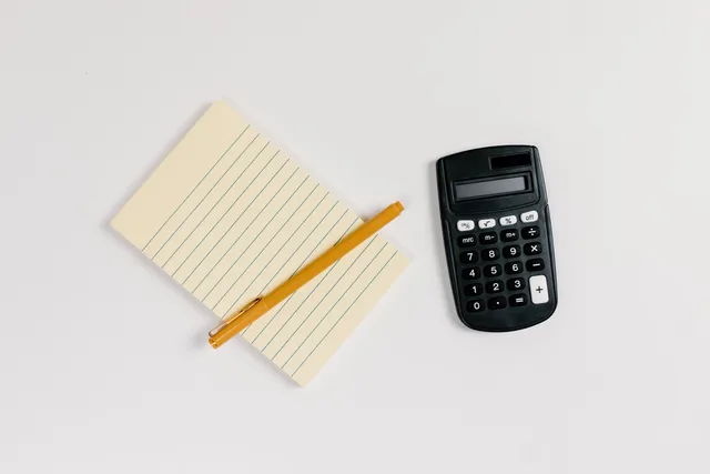Minimalist flat lay of a calculator and lined notepad with a gold pen on a white surface. Email marketing software pricing models: a buyer's worksheet